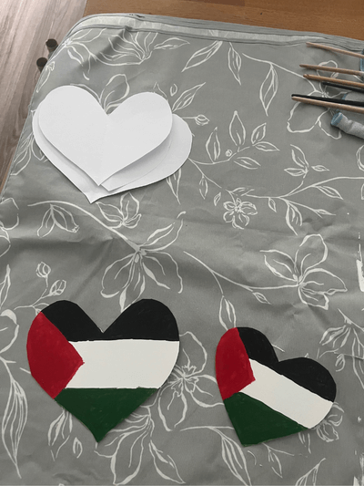 Zwei gemalte Herzen in den Farben der Palästina-Flagge mit dem Text: Herzen für Palästina. Menschlichkeit braucht eine Stimme