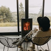 rau mit Hut sitzend vor Kaminfeuer und leerer Stuhl links