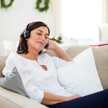 Frau trägt Kopfhörer und sitzt entspannt mit geschlossenen Augen auf Sofa