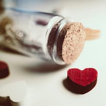 Flasche mit Message darin und daneben liegendem roten Herz aus Holz