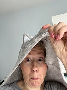 Jana Engel schaut unter ihrer Decke hervor - Verstecken war gestern. Jana Engel Seelenguide schaut lustig unter einer Decke hervor, die wie ein Katzenkopf aussieht. Denn das Motto für 2025 lautet: Raus in die Welt!
