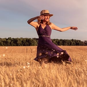 Frau in Sommerkleid mit Hut tanzt über sommerliche Wiese