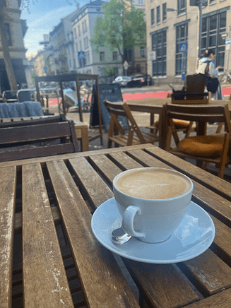 Die erste Tasse draußen. Ein zarter Auftakt: Wärme auf der Haut, Kaffee in der Hand, Frühling in der Luft. Tasse Kaffee draußen auf Holztisch, erstes Mal im Freien im April 2025