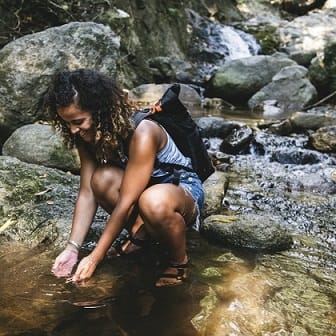 Frau mit Rucksack schöpft Wasser aus Quelle