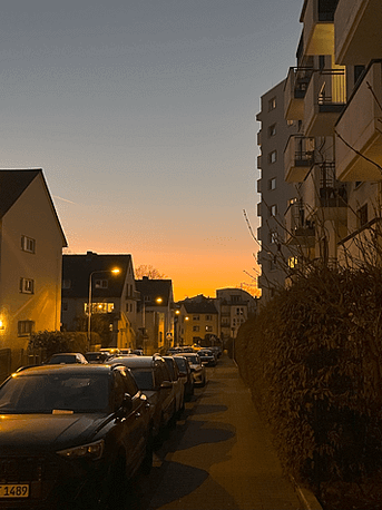 Orangefarbener Sonnenuntergang über den Häusern auf dem Nachhauseweg von der Arbeit – ein Zeichen dafür, dass es abends länger hell bleibt
