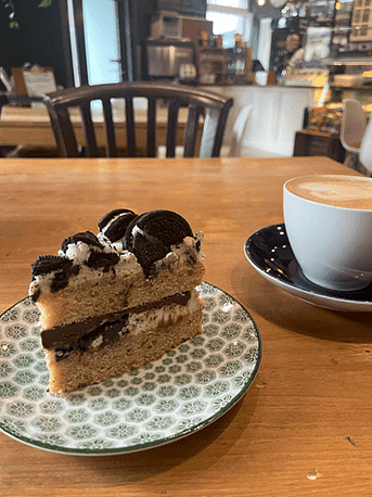 Ein Teller mit Oreo-Cookie-Kuchen und ein Cappuccino im Matildas – Feiermoment nach der Fertigstellung des Imbolc-Workbooks
