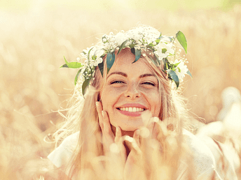 Frau mit Blumenkranz im Haar lacht auf einem blühenden Feld – Sinnbild für Lebenslust und Freiheit zu Beltane