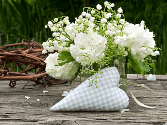 Herz und Maiglöckchen auf rustikalem Holztisch – Sinnbild für Liebe, Segen und Neubeginn zu Beltane