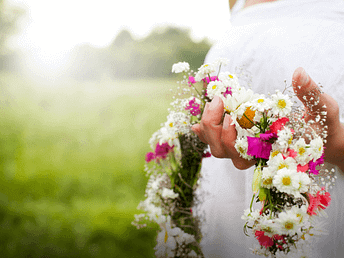 Hände halten einen Blumenkranz aus weißen und grünen Blüten – Symbol für Segen, Schönheit und Erblühen zu Beltane