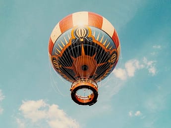 Orange-weißer Heißluftballon der in den blauen Himmel aufsteigt