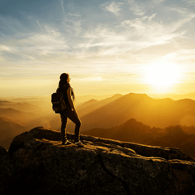 Frau steht kraftvoll auf einem Felsen und blickt in den Sonnenuntergang - Symbol für Klarheit, Entscheidung und Stärke