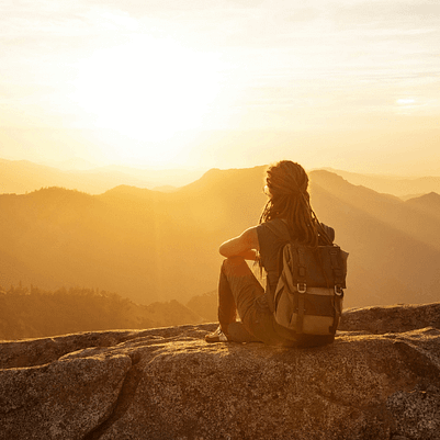 Frau sitzt ruhig in den Bergen bei Sonnenaufgang und blickt in die Weite -Symbol für den Moment vor der Klarheit