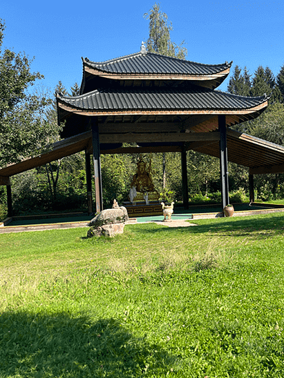 Blick über Wiese zu überdachtem Buddha