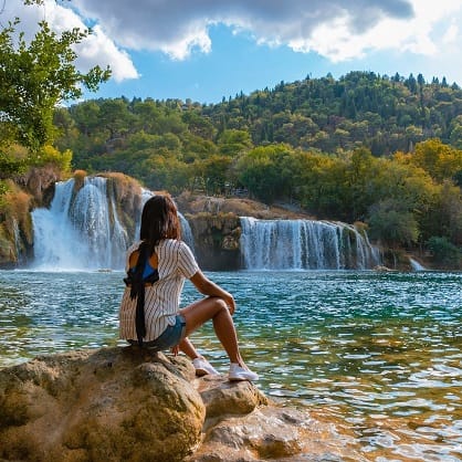 Frau sitzt an See mit Wasserfall