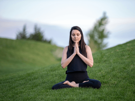 Frau in Yoga-Haltung auf einer Wiese - Meditation und Achtsamkeit als Weg zur Lebensaufgabe finden