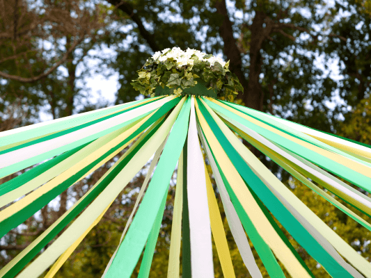 Beltane – Maibaum und Blumenkranz Maibaum mit grün-gelben Bändern und Blumenkranz – Symbol für Fruchtbarkeit, Lebenskraft und das Erblühen zu Beltane