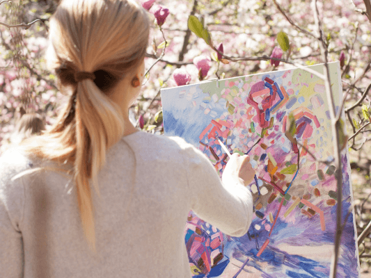 Frau malt im Freien inmitten blühender Bäume - Ausdruck von Kreativität ohne Leistungsdruck Frau malt im Freien inmitten blühender Bäume - Ausdruck von Kreativität ohne Leistungsdruck