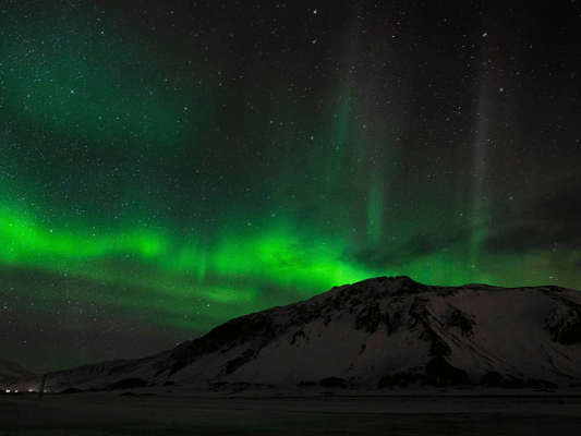 Grüne Nordlichter über verschneitem Berg - Himmelsphänomen durch Sonnenaktivität