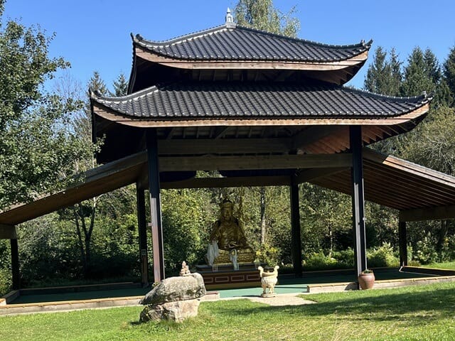 Blick auf die Meditationshalle des Klosters Buddhas Weg, umgeben von Natur unter blauem Himmel