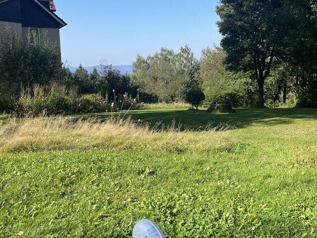 Blick am Kloster Buddhas Weg über eine grüne Wiese und blauen Himmel, mit meiner Schuhspitze im Vordergrund