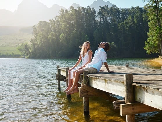 Paar aus Mann und Frau sitzt auf einem Steg am See und lacht