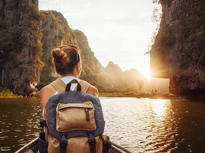 hingabe-loslassen-vertrauen-ins-leben-jana-engel-coaching-beratung-mut-selbstvertrauen-orientierung-selbstfindung-einzigartigkeit-dem-fluss-des-lebens-folgen-innerer-kompass Frau mit Rucksack sitzt in Boot und schaut auf Sonnenuntergang