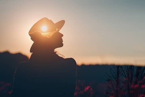 Silhouette junge Frau mit Hut vor Sonnenaufgang