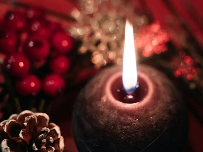 Einfaches Kerzenritual für die Rauhnächte Eine brennende Kerze mit Tannenzapfen und Dekoration - eine einfache Möglichkeit, die Rauhnächte zu feiern