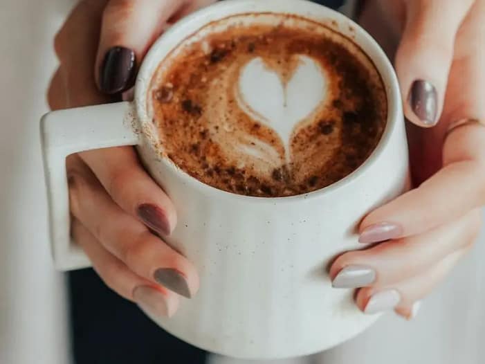 Hände, die eine Tasse mit Herz-Latte-Art halten - ein Moment der Wärme, Geborgenheit und Intuition auf dem Weg zum eigenen Claim.