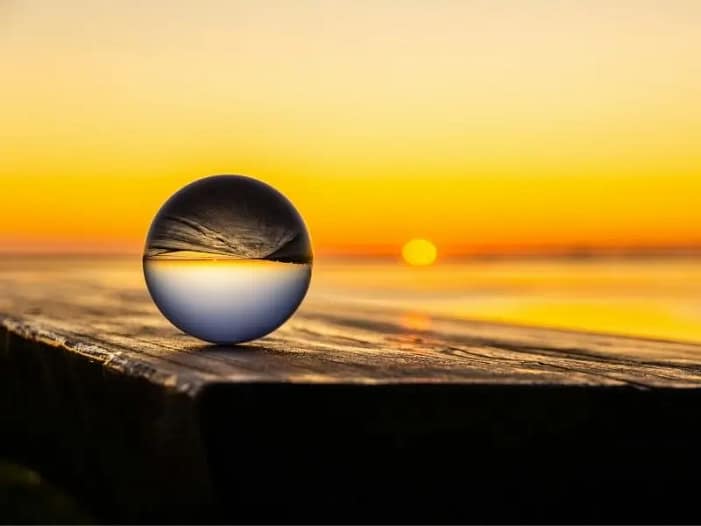 Glaskugel reflektiert Sonnenuntergang - Human Design als Spiegel auf dem Weg zur Lebensaufgabe Glaskugel auf Holz reflektiert einen goldenen Sonnenuntergang am Meer - Sinnbild für Selbstreflexion und Human Design als Spiegel auf dem Weg zur eigenen Lebensaufgabe