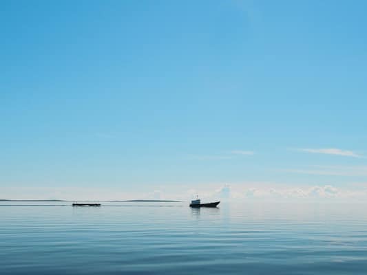 Ruhiges Meer mit kleinem Fischerboot unter blauem Himmel – Symbol für innere Balance & entspannten Umgang mit Emotionen
