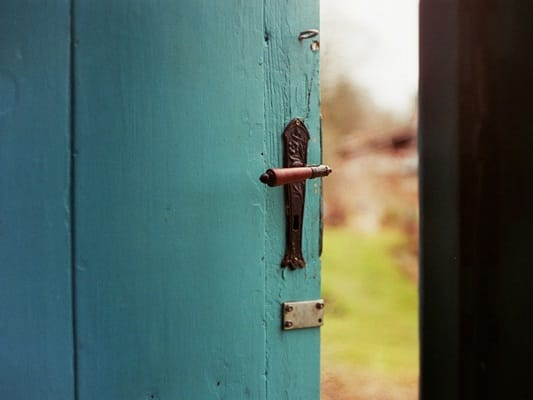 Halboffene türkisfarbene Tür mit Blick ins Grüne – Symbol für bewusstes Grenzen setzen