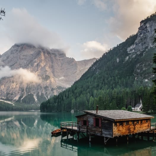 raum-fuer-dich-ruhe-atmen-ankommen-sein-selbstfindung-verbindung-bestandsaufnahme-reflektion-resonanz-energie-wunderbares-entsteht-wohnen-am-see-jana-engel Holzhaus im See vor Berghintergrund