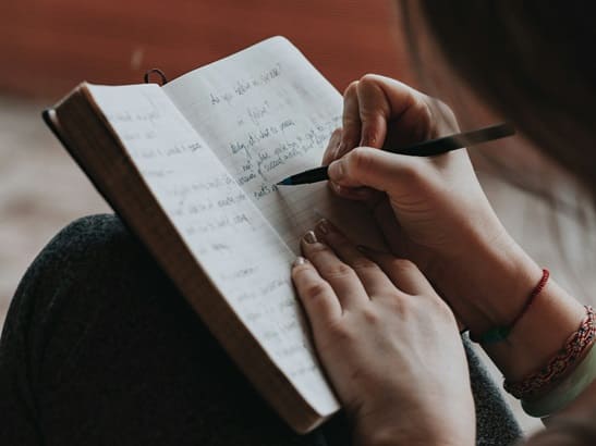 Weibliche Hände. Eine Hand hält Stift und schreibt in Notizbuch.