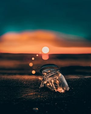 Glasdose mit Lichterkette bei Sonnenaufgang am Strand